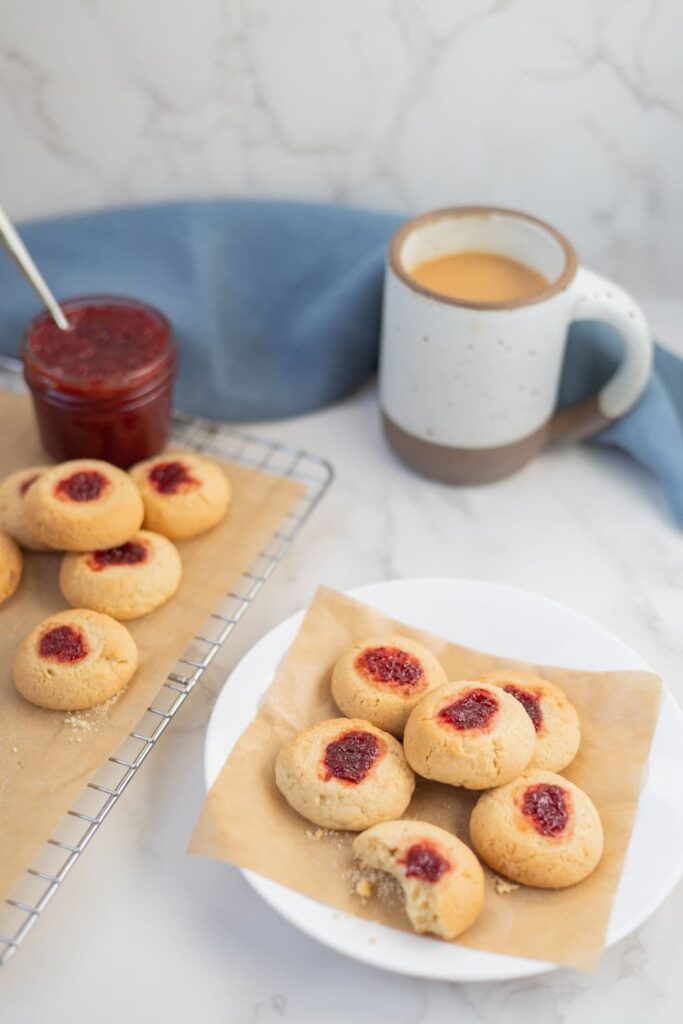 A plate of sourdough thumbprint cookies sitting in front of a cup of coffee.