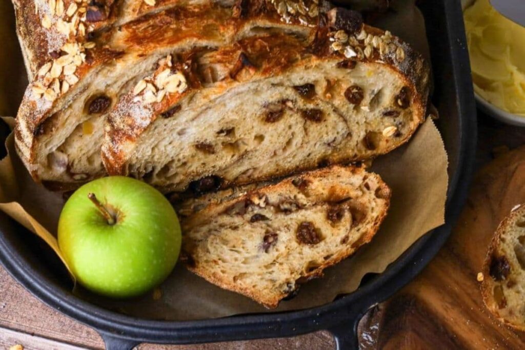 A loaf of sourdough apple crisp bread in a pan, sliced and focused on texture, showing raisins.