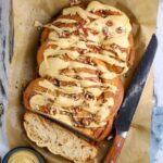 A close up overhead view of a sourdough maple pecan twist loaf with glaze topping and one slice to show inside texture.