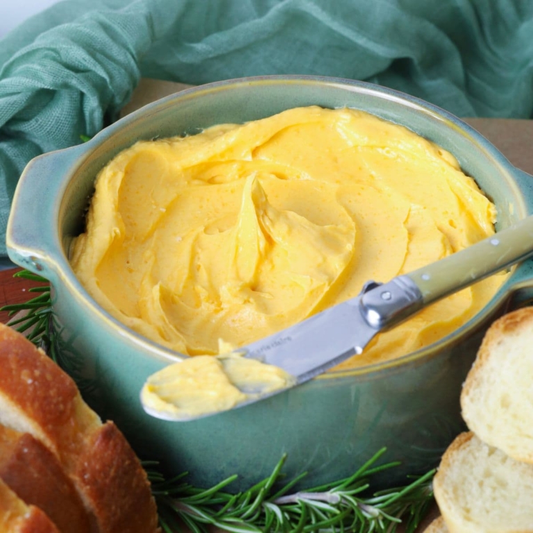 Close up of cheddar butter in a serving bowl with a butter knife for spreading onto bread.